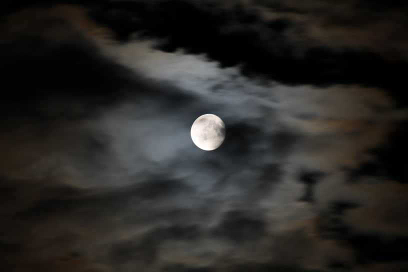 Vollmond hinter grauem Himmel mit dunklen Wolken