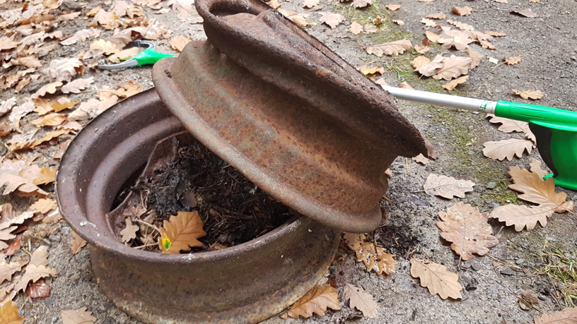 Zwei Autofelgen übereinander liegen auf dem Waldweg, darauf liegt der Müllgreifer.