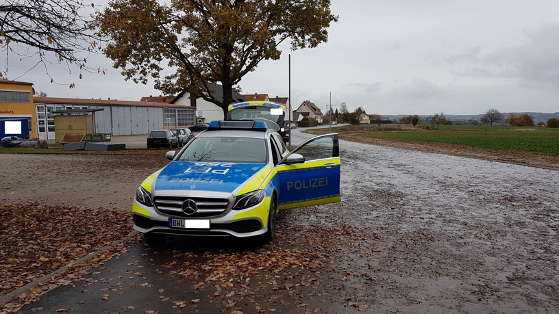 Polizeifahrzeug mit offener Fahrertüre und geöffnetem Kofferraum steht auf der Fahrbahn. Das Kennzeichen ist teilweise unkenntlich gemacht.