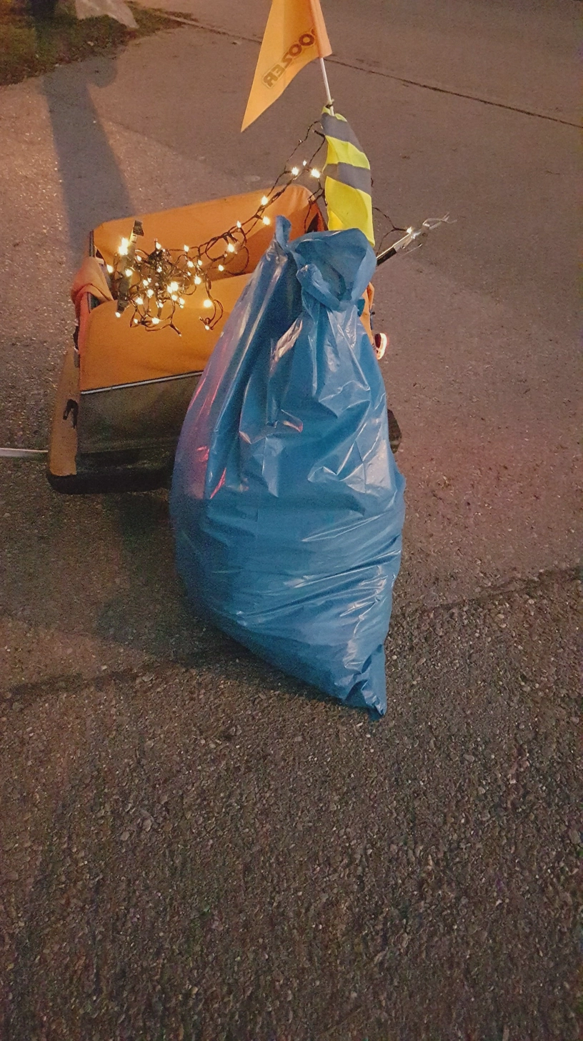 Blauer Müllsack steht vor dem Anhänger, an dem eine eingeschaltete Lichterkette hängt.