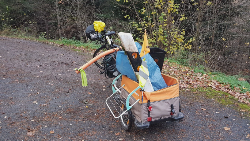 Fahrrad mit Anhänger und verschiedenem gesammelten Müll darin, unter anderem der Leitpfosten.