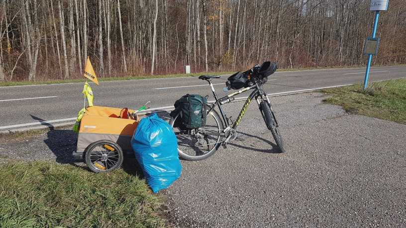 Gespann aus Fahrrad und Fahrradanhänger, vor dem Anhänger steht ein voller Müllsack.