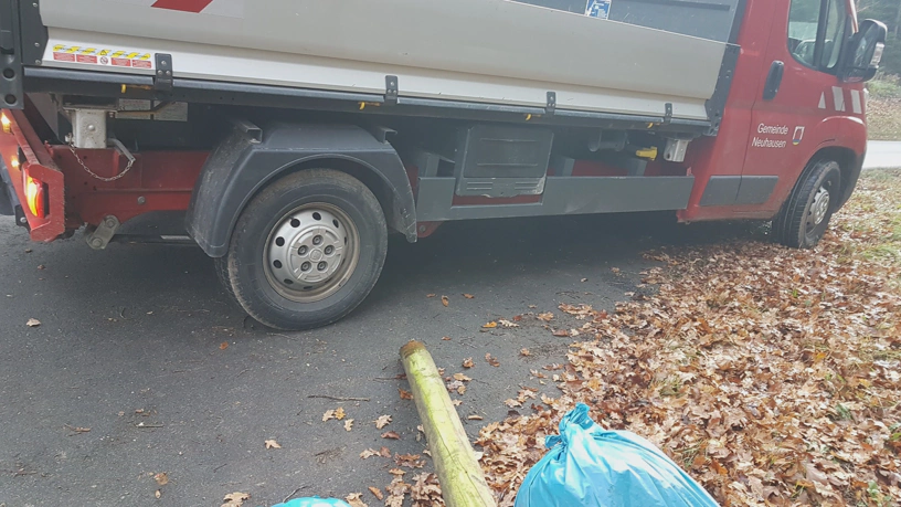 Fahrzeug mit Ladefläche steht am Waldrand. Am unteren Bildrand der gesammelte Müll in Müllsäcken teilweise erkennbar.