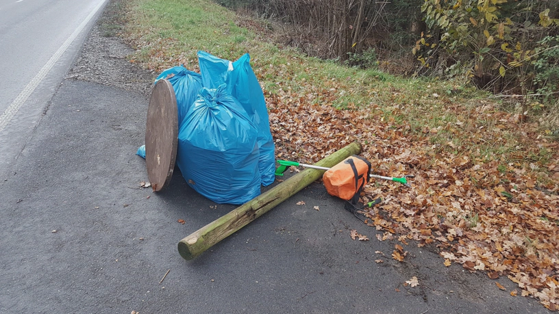 Mehrere Müllsäcke, eine runde Tischplatte und ein Pfahl, der Müllgreifer und der faltbare Mülleimer liegen am Straßenrand.