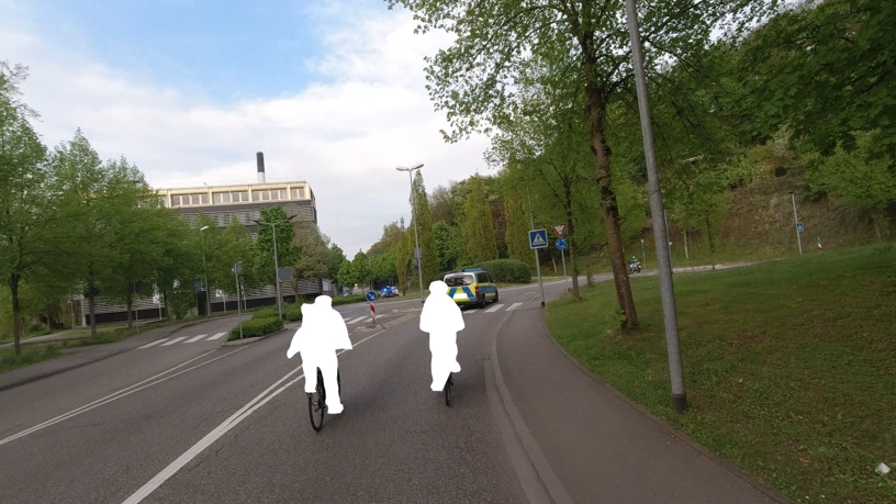 Kreisverkehr. Links im eigenen Fahrstreifen stand später der Fahrer mit seinem Lkw. Kreisverkehr. Links ein eigener Fahrstreifen zum Vorbeifahren am Kreisverkehr. Vor mir zwei Radfahrende, unekenntlich gemacht und vor diesen ein Polizeiauto. Im Kreisverkehr sperren zwei Motorradpolizisten die Einfahrten ab.