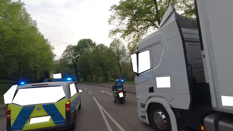 Rechts der stehende Lkw und Polizei davor. Von der Kamera eines Radfahrers. Auf dem Fahrstreifen rechts steht der Lkw, etwas davor ein Motorrad mit Polizist drauf und blaulicht, auf dem Fahrstreifen vor dem Radfahrer ein Polizeiauto mit Blaulicht.