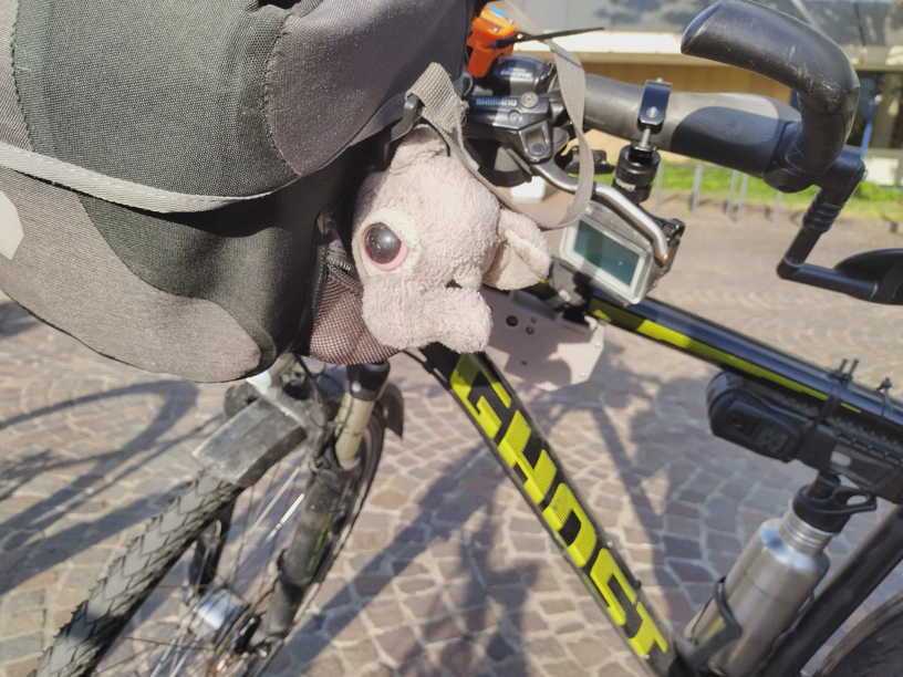 Der kleine Elefant in der Seitentasche der Lenkertasche und schaut in die Kamera. Dahinter und darunter sind der gepflasterte Boden des Waisenhausplatzes zu sehen und Teile des Kongresszentrums Pforzheim.