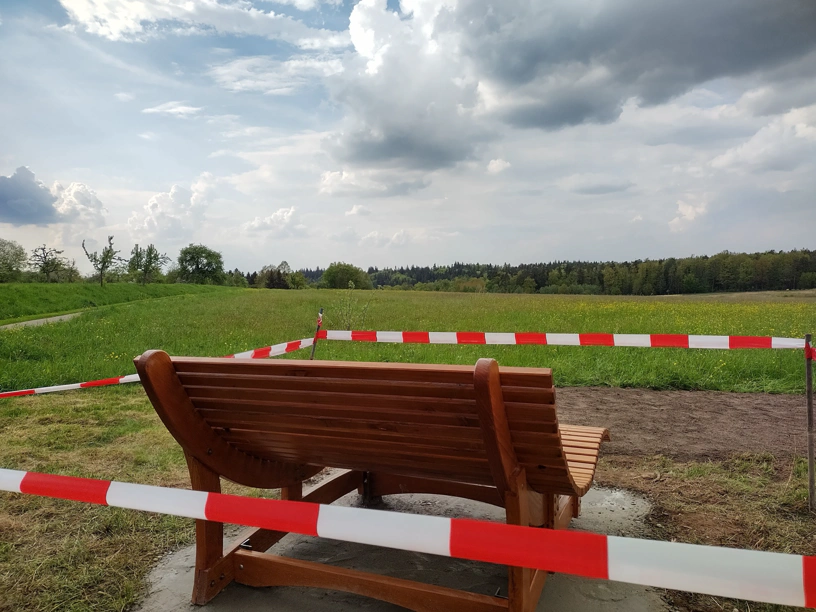 Die Liegebank von hinten Fotografiert mit Blick auf die Landschaft, die man auf der Bank sitzend betrachten kann. Weite Wiese und Wald dahinter.