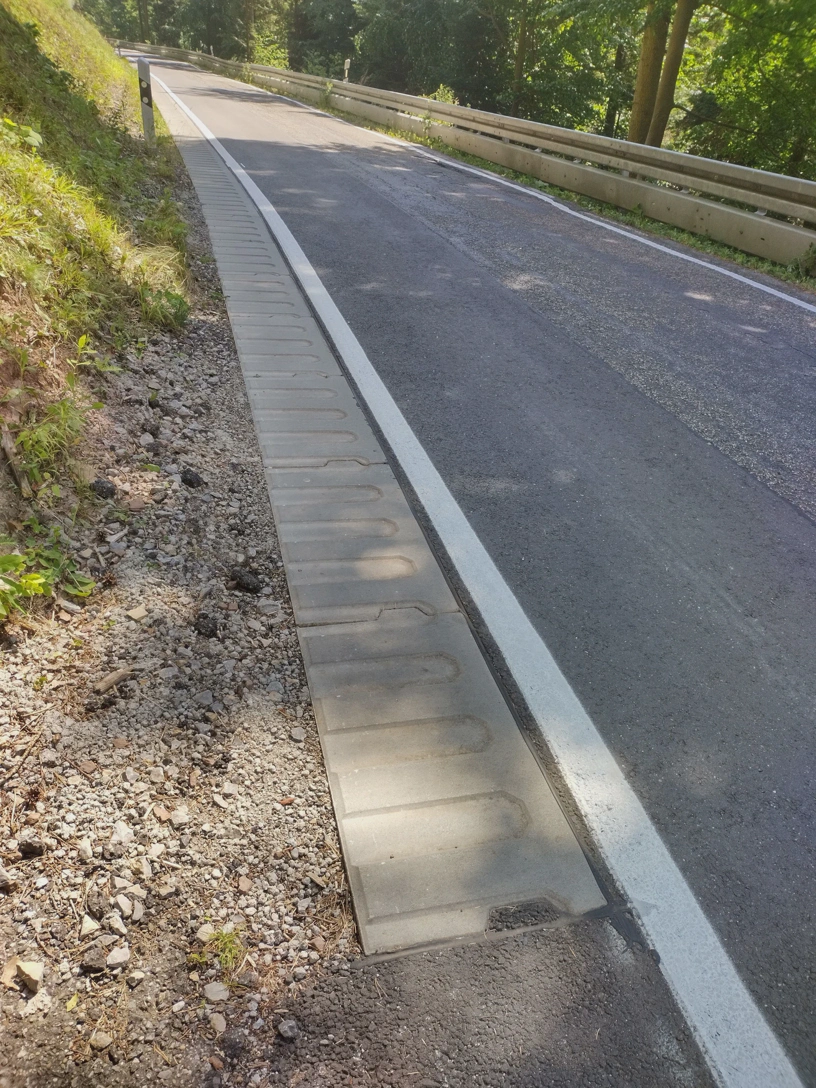 Schmale Landstraße mit Platten am Fahrbahnrand, die in der Mitte eine Vertiefung haben.