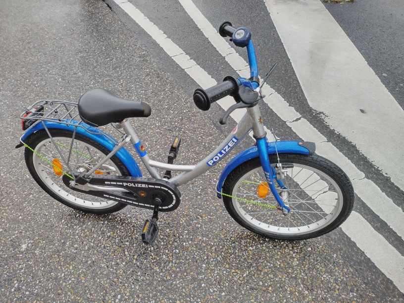 Ein blau, graues Kinderfahrrad mit der Aufschrift Polizei. Dazu mehrere Wappen.