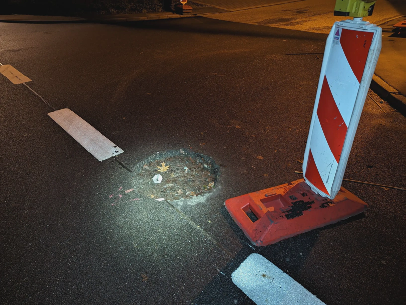 Foto der Gefahrenstelle. Kreuzungsbereich, neben dem Loch mit ca. 0,5 m Durchmesser und ca. 10 cm Tiefe steht die Bake. Das ist der Zustand vor der Verschiebung der Bake. 